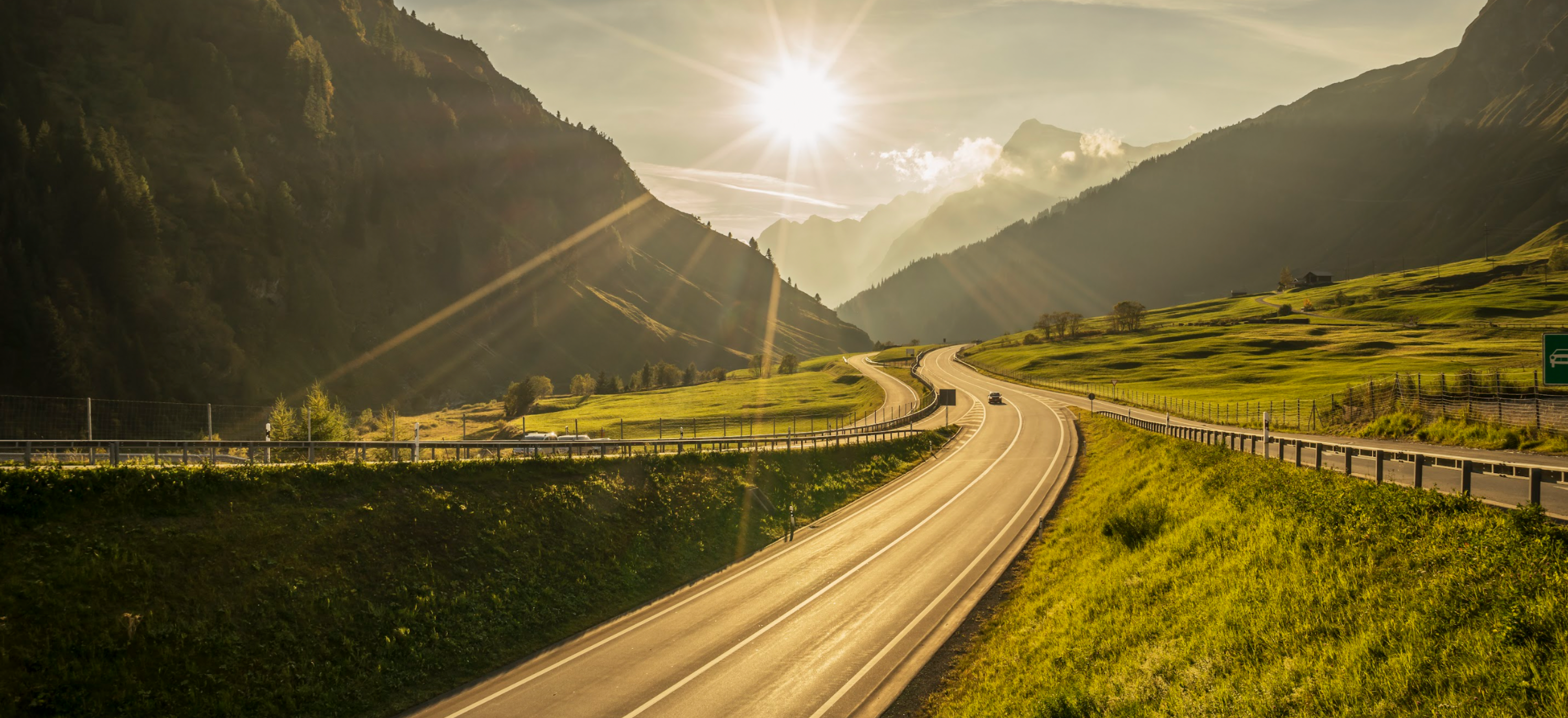 Image of a winding road on a countryside landscape near sunset.