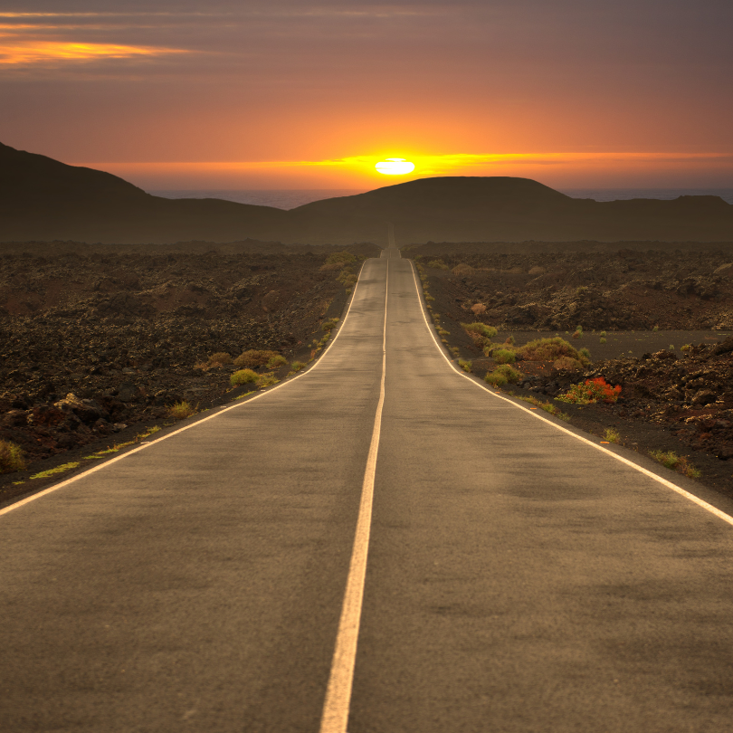 An empty road extends far ahead, surrounded by vast landscapes, inviting solitude and reflection.