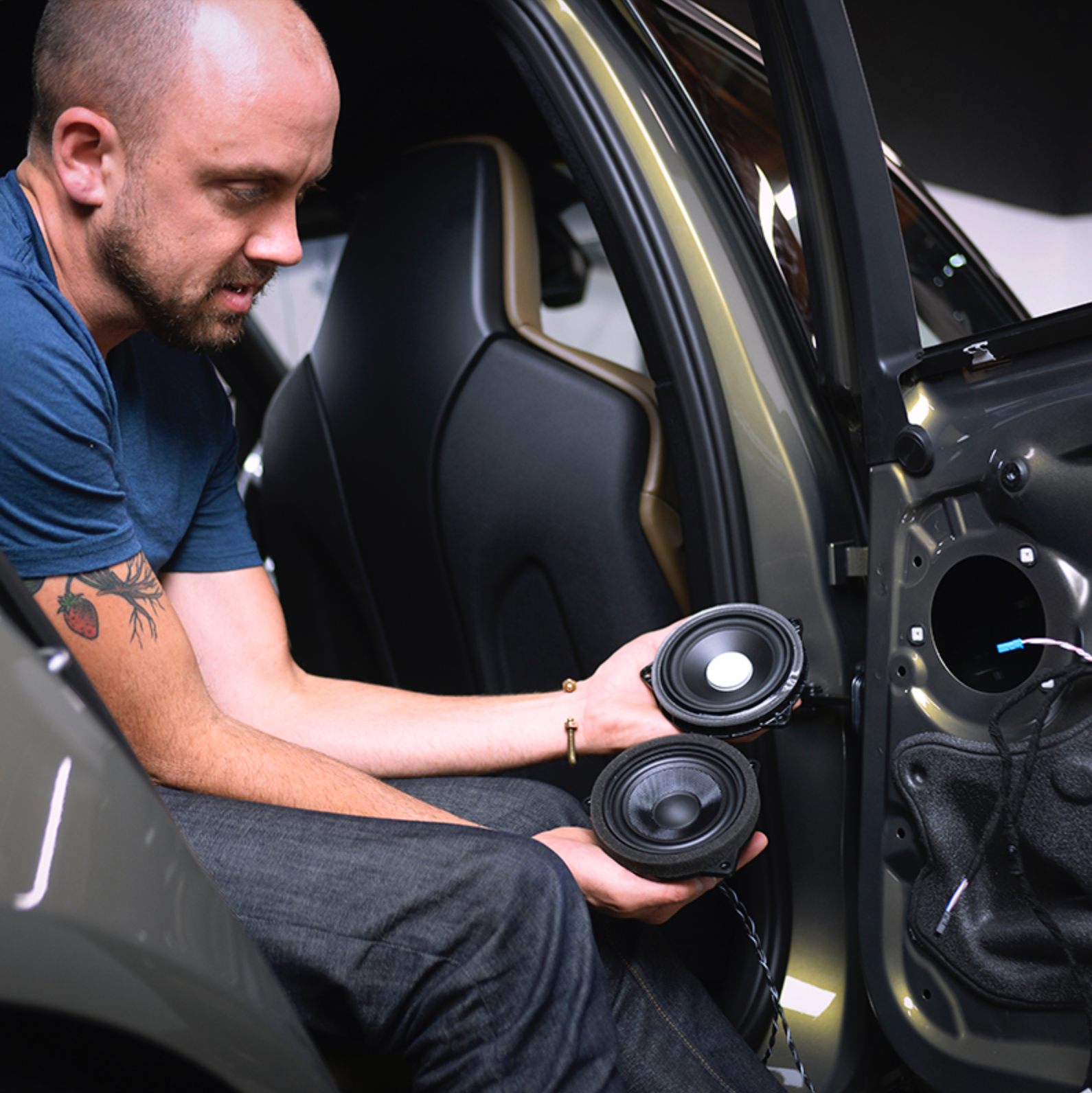 Man holding a Bavsound mid-range speaker next to a factory speaker showing the increase in build quality and materials. 